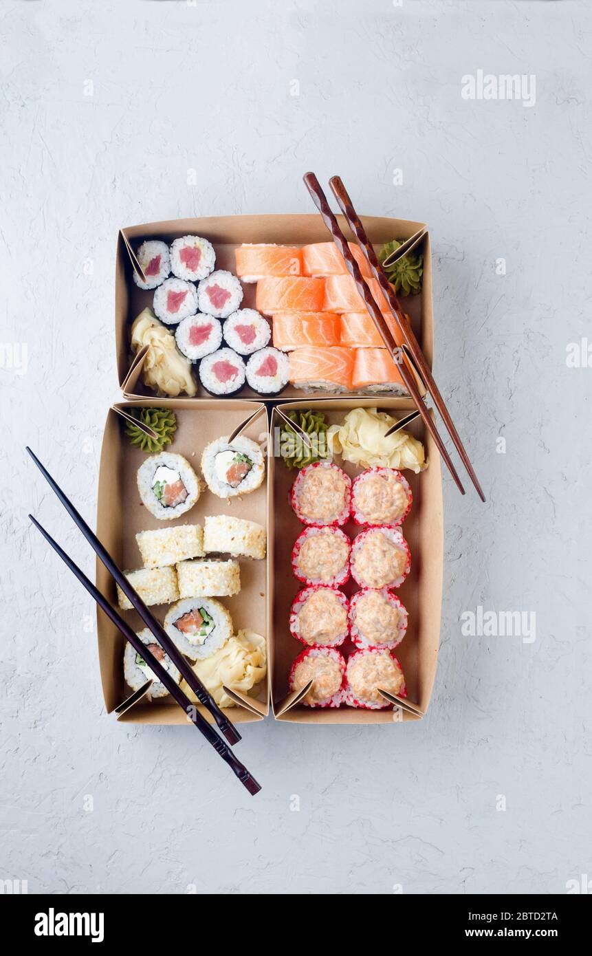 Leckere Sushi-Rollen in Einweg-Kraftpapier-Boxen, Sauce auf dunklem Tisch. Konzept Lieferservice Japan Lebensmittel in Öko-Container. Flaches Lay, Schablone Mocku Stockfoto