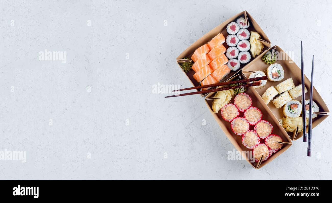 Leckere Sushi-Rollen in Einweg-Kraftpapier-Boxen, Sauce auf dunklem Tisch. Konzept Lieferservice Japan Lebensmittel in Öko-Container. Flaches Lay, Schablone Mocku Stockfoto