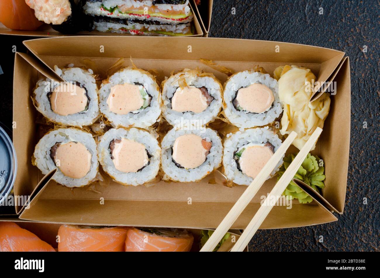 Leckere Sushi-Rollen in Einweg-Kraftpapier-Boxen, Saucen auf dunklem Tisch. Konzept Lieferservice Japan Lebensmittel in Öko-Container. Flach legen, Vorlage Mock Stockfoto