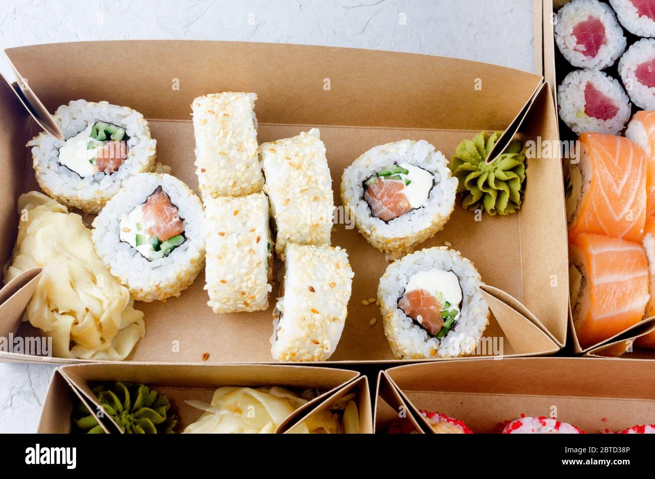 Leckere Sushi-Rollen in Einweg-Kraftpapier-Boxen, Sauce auf dunklem Tisch. Konzept Lieferservice Japan Lebensmittel in Öko-Container. Flaches Lay, Schablone Mocku Stockfoto