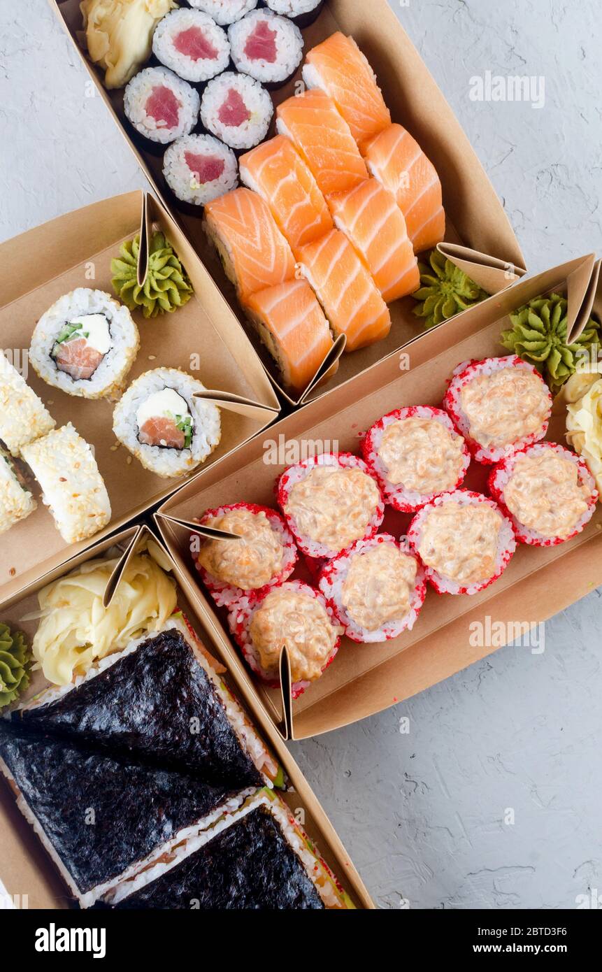 Leckere Sushi-Rollen in Einweg-Kraftpapier-Boxen, Sauce auf dunklem Tisch. Konzept Lieferservice Japan Lebensmittel in Öko-Container. Flaches Lay, Schablone Mocku Stockfoto