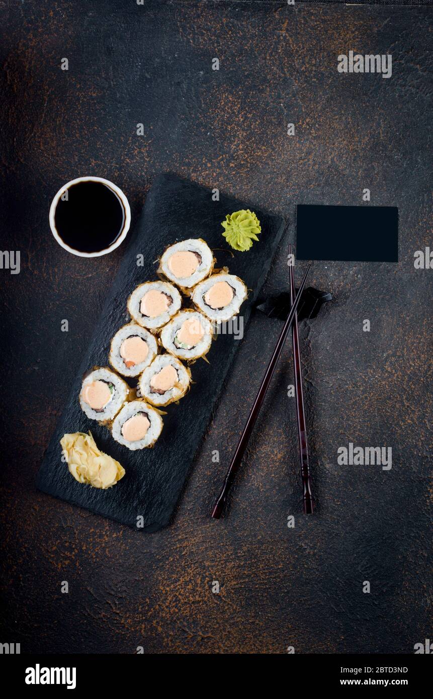 Leckere Rollen philadelphia in Thunfisch auf Steinplatte mit Saucen, Essstäbchen, Ingwer und Wasabi auf dunklem Tisch. Asiatische Küche. Lieferservice Japanisches Essen . Stockfoto