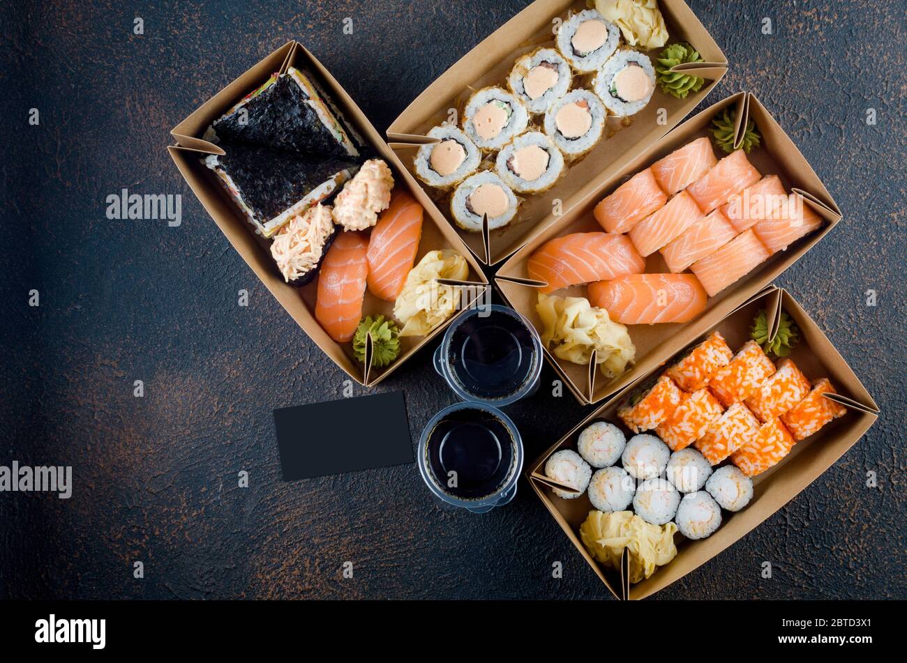 Leckere Sushi-Rollen in Einweg-Kraftpapier-Boxen, Saucen auf dunklem Tisch. Konzept Lieferservice Japan Lebensmittel in Öko-Container. Flach legen, Vorlage Mock Stockfoto
