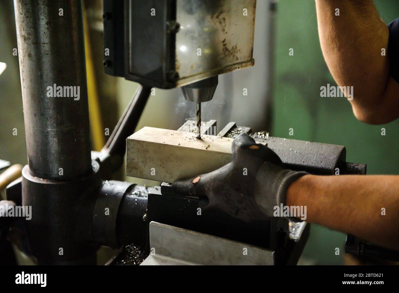 Arbeiter bohren einen Aluminiumblock auf einer großen industriellen Bohrmaschine in einer Werkstatt in der Nähe seiner Handschuhhandschuhen Stockfoto
