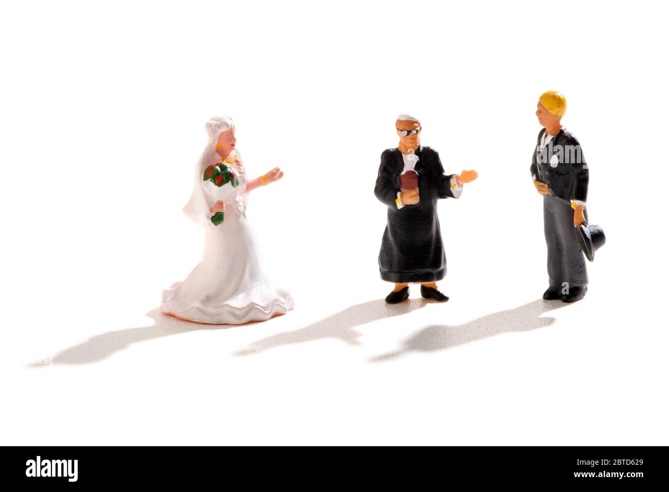 Miniatur-Hochzeit Szene mit Brautpaar und Priester soziale Distanzierung während der Zeremonie mit Schatten über einem weißen Hintergrund konzeptuelle Liebe und Stockfoto