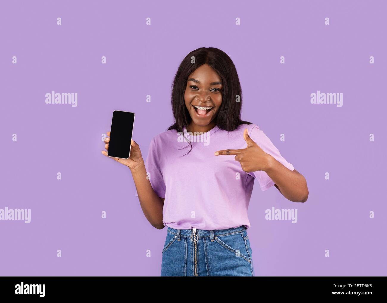 Cool schwarzes Mädchen zeigt auf leere Handy-Bildschirm auf lila Hintergrund, kopieren Raum Stockfoto