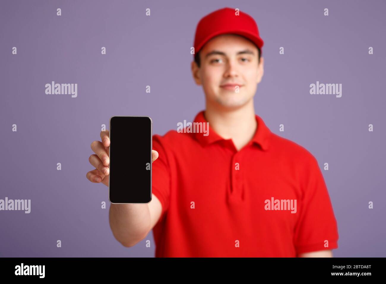 Sparen Sie Zeit bei der Lieferung. Freundlicher Kurier in Uniform zeigt Smartphone mit leerem Bildschirm Stockfoto