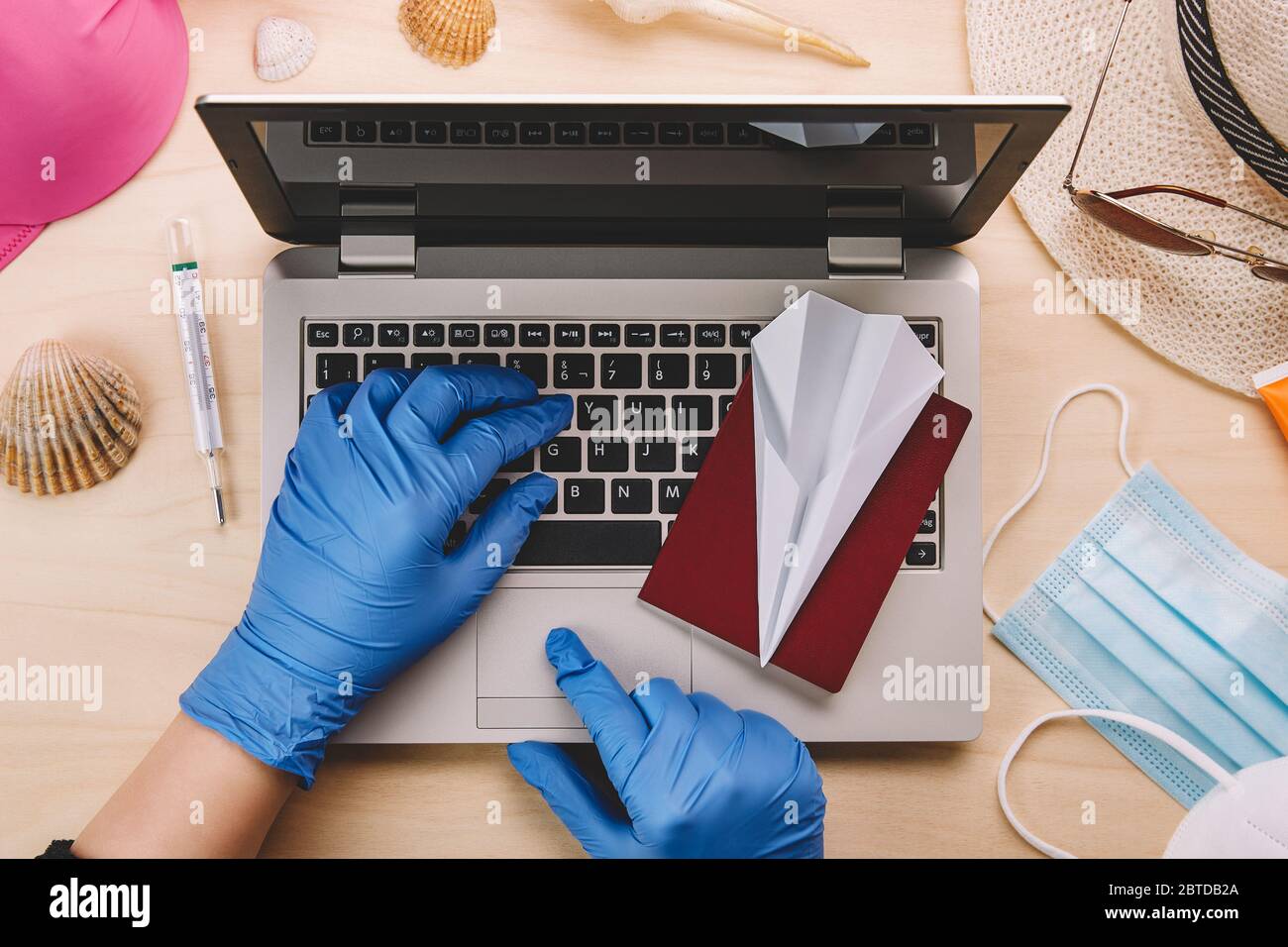 Coronavirus und Reisekonzept. Frau mit blauen Latexhandschuhen, die einen Laptop benutzen, um Sommerferien während der Coronavirus-Pandemie zu buchen. Flaches Lay Stockfoto