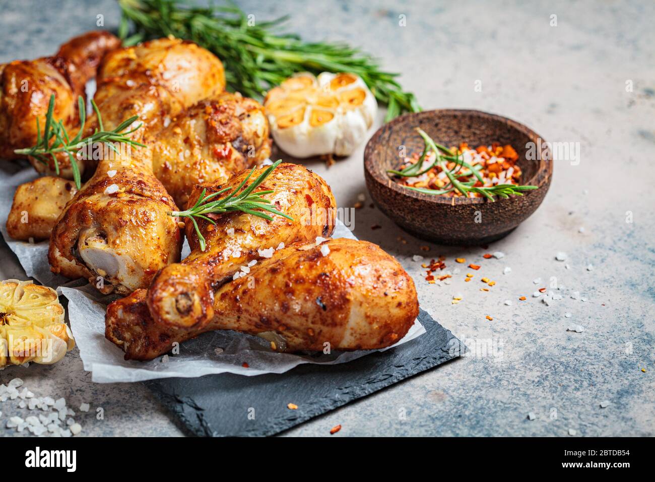 Gebratene würzige Hähnchenbeine mit Kräutern und Knoblauch auf schwarzem Schiefer, dunkler Hintergrund. Stockfoto