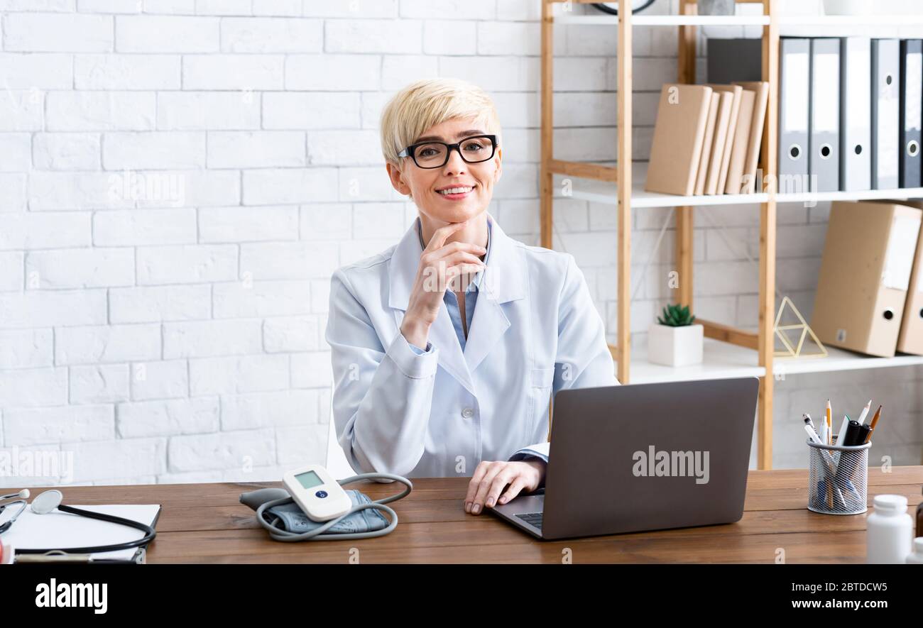 Erschwingliche Behandlung. Lächelnde Frau Arzt sitzt am Tisch Stockfoto