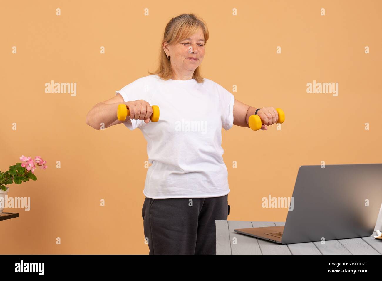 Frau mit Laptop zu Hause beobachten Fitness-Videos Online-Training mit gelben Hanteln Stockfoto