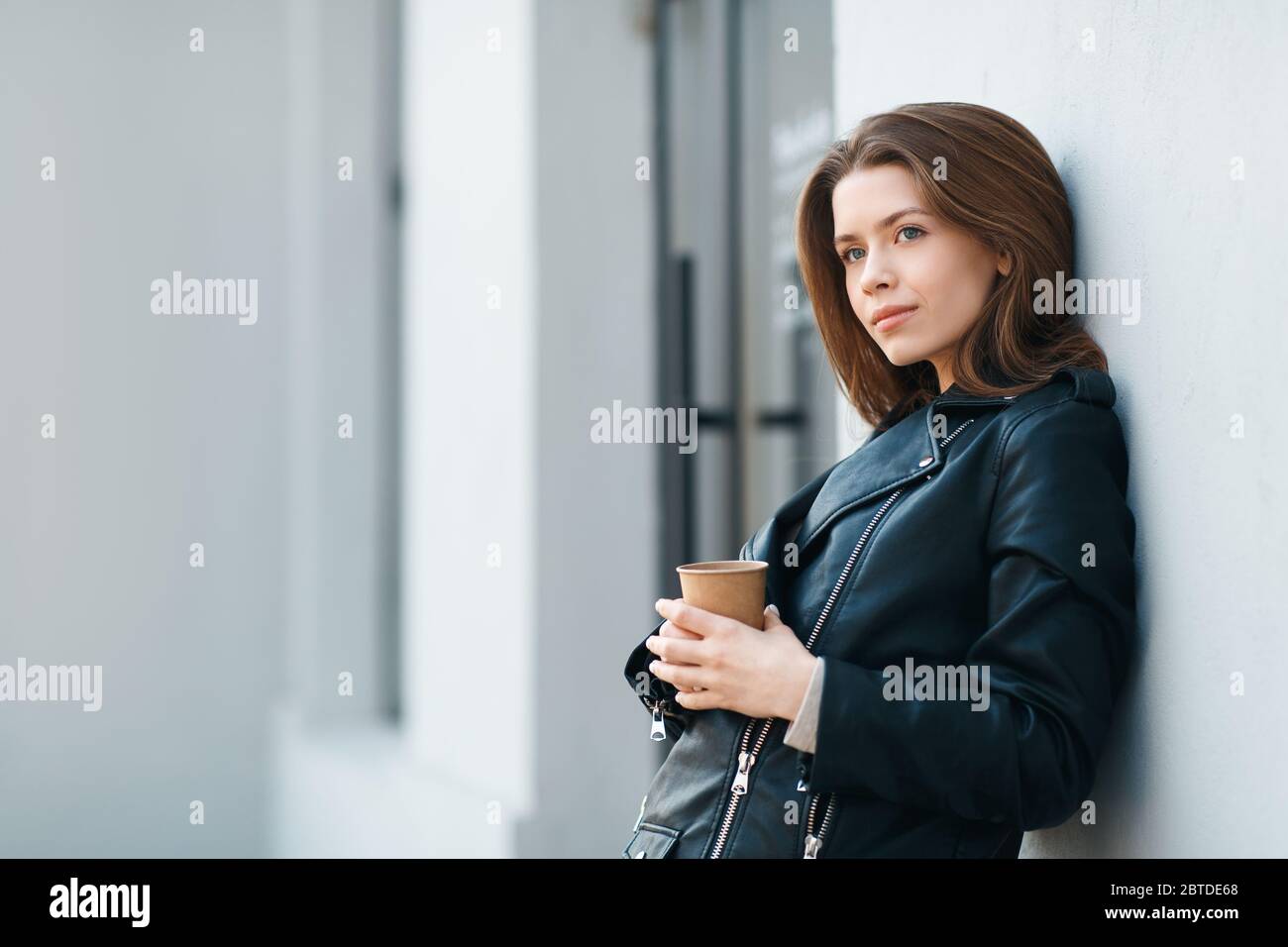 Glücklich casual brünette weiblich Aufenthalt in der Nähe von grauen Wand mit Kaffee Stockfoto