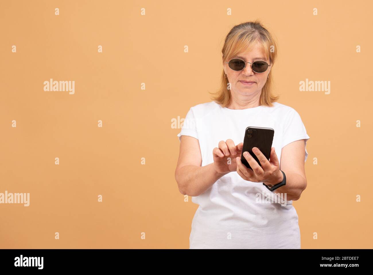 Glückliche ältere Frau in Sonnenbrille hält Smartphone mit mobilen Online-Apps, lächelnd alte Dame mittleren Alters SMS-Nachricht chatten auf Stockfoto