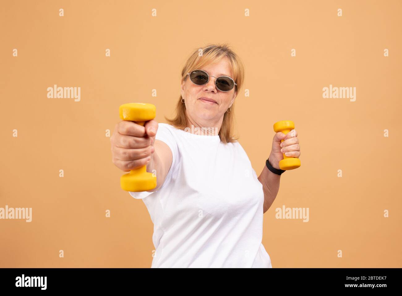 Aufgeregt Senior Fitness Frau in Sonnenbrillen Training mit Kurzhanteln isoliert auf orange Stockfoto
