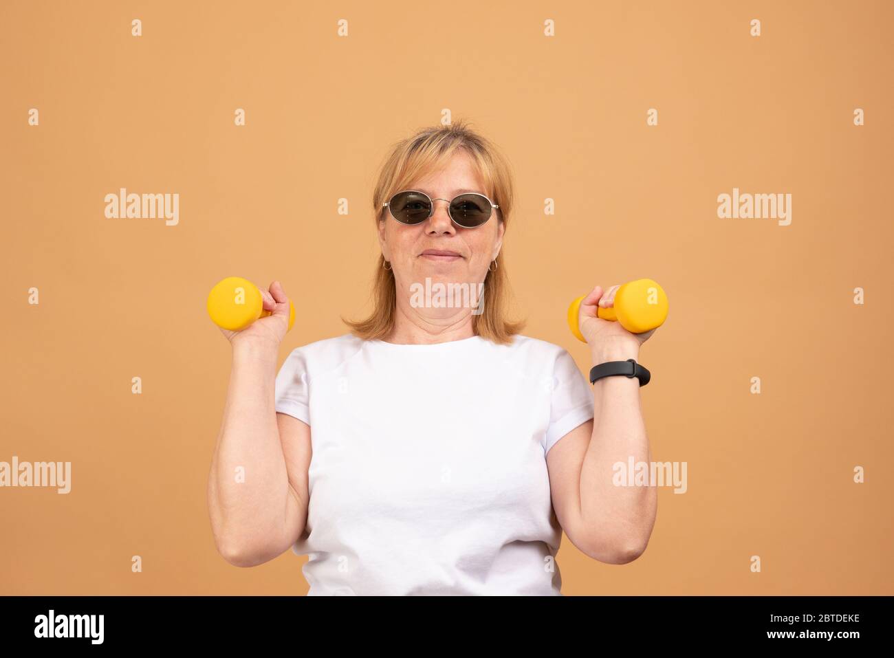 Menschen, Alter, Sport und aktives Lifestyle-Konzept. Bild von glücklichen positiven reifen Frau im Ruhestand in T-Shirt tun Übung mit freien Gewichten im Fitnessstudio Stockfoto
