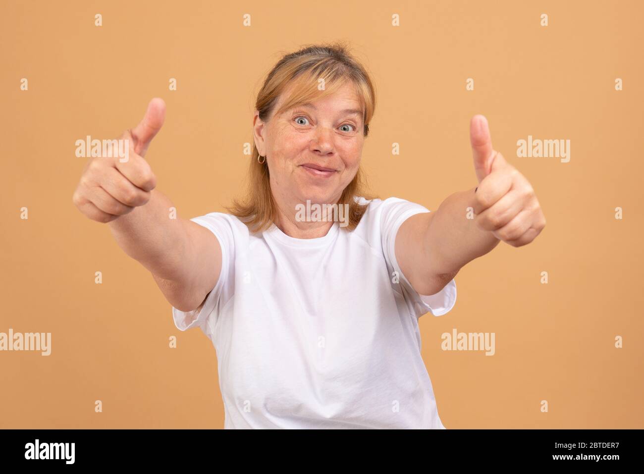 Lächelnd reife Frau in T-Shirt isoliert auf orangen Studio Hintergrund zeigen Daumen nach oben empfehlen Service Stockfoto