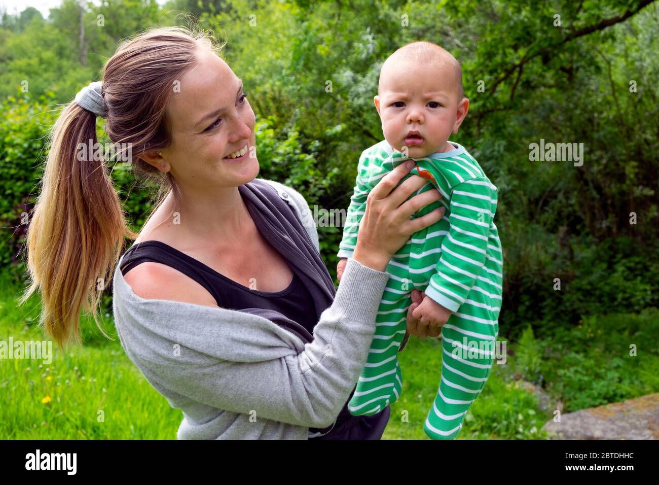 Hübsche Mutter hält 3 Monate Baby draußen in einem grünen Garten im Mai Wetter Frühling Sonnenschein während covid 19 Pandemie 2020 UK KATHY DEWITT Stockfoto