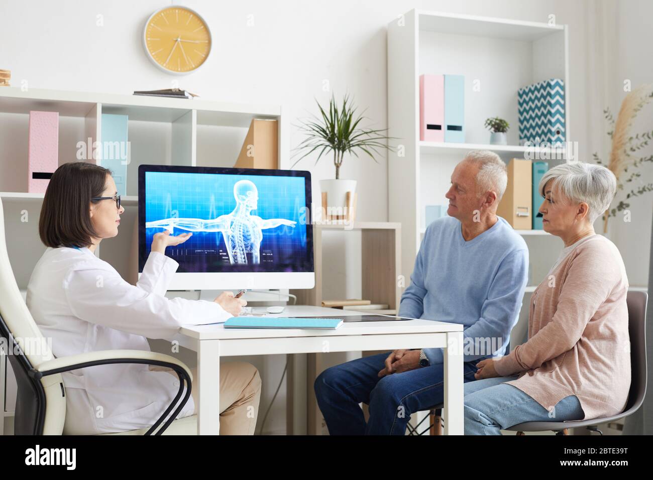 Porträt des modernen älteren Paar hört auf Ärztin und Blick auf Röntgenbild während der Konsultation in der Klinik Stockfoto