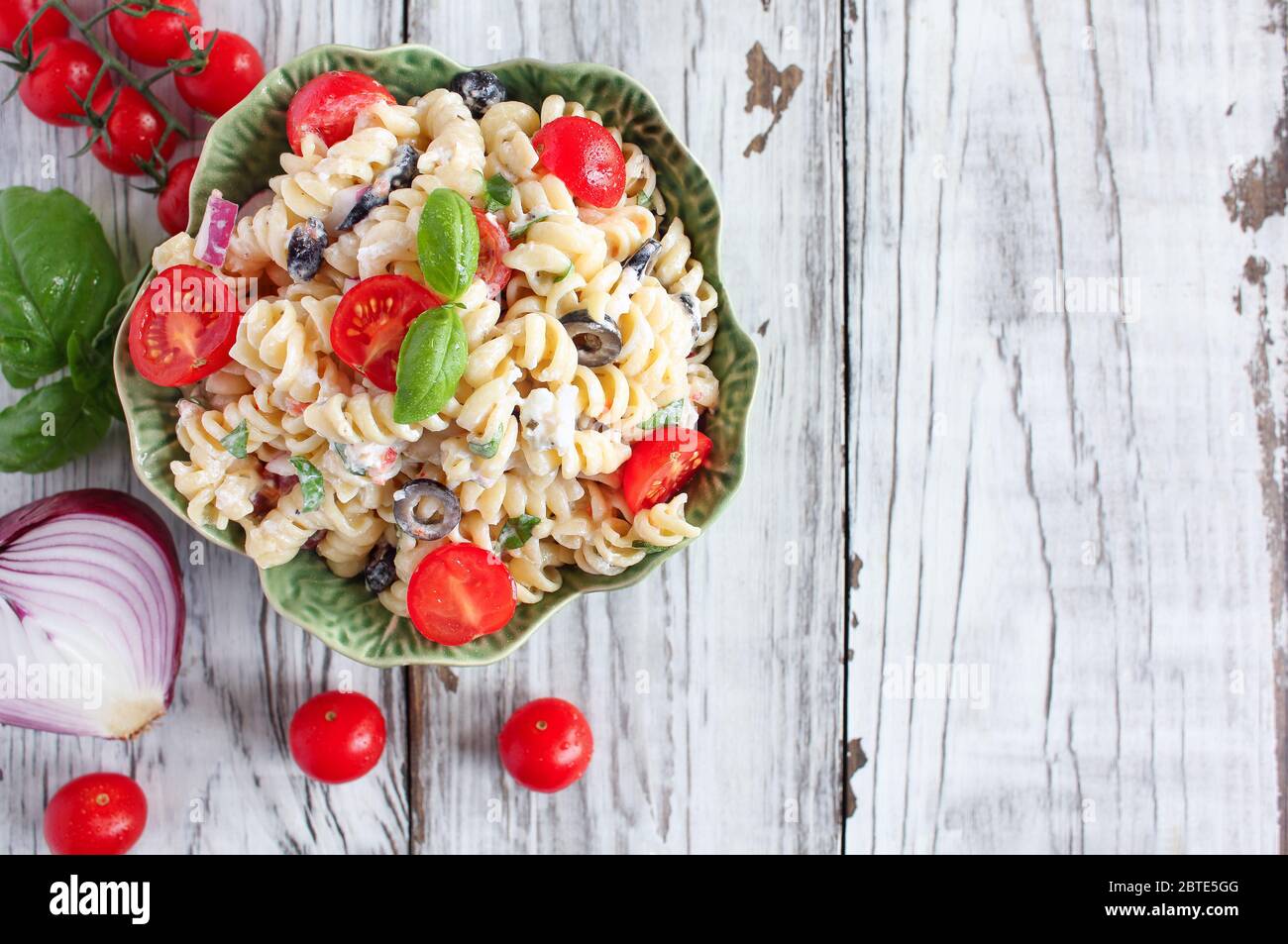 Von oben gesehen: Pasta-Salat mit frisch gehacktem Basilikum, Tomaten, schwarzen Oliven, roten Zwiebeln und Feta-Käse, mit einem italienischen Öldressing. Stockfoto