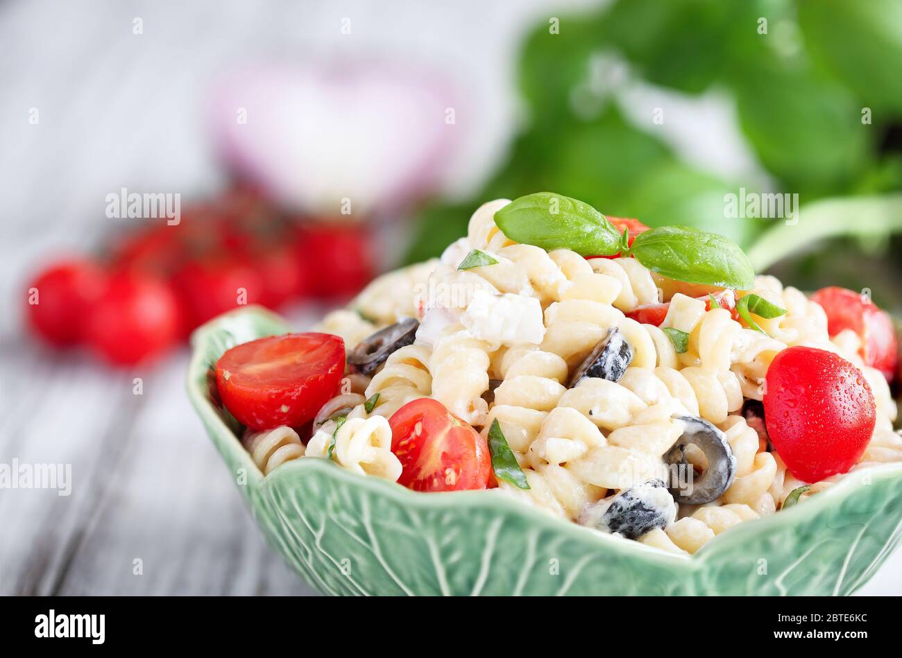 Pasta Salat mit frisch gehacktem Basilikum, Tomaten, schwarzen Oliven, roten Zwiebeln und Feta-Käse, mit einem italienischen Öl-Dressing geworfen. Stockfoto