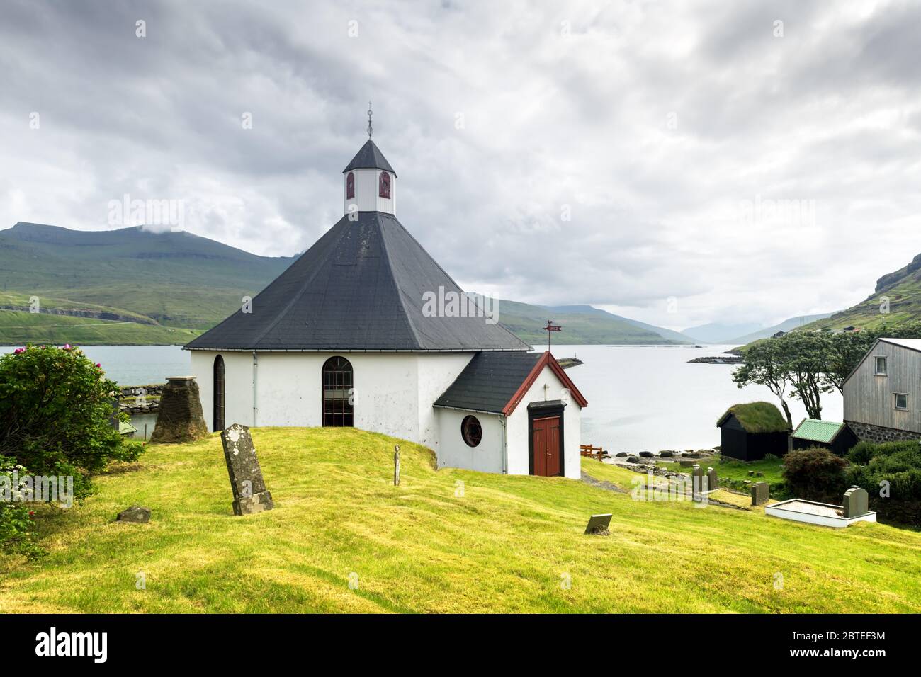 Sommer Blick auf die traditionelle Kirche in faroese Dorf. Schöne Landschaft mit nebeligen Fjord und hohen Bergen. Färöer, Dänemark. Stockfoto