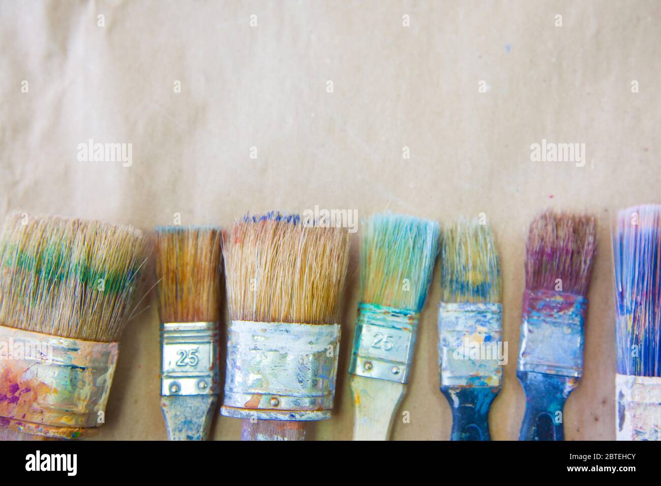 Schmutzige gebrauchte Künstlerpinsel liegen in einer Reihe oder Linie. Hintergrund beige Papier Kraft. Stockfoto