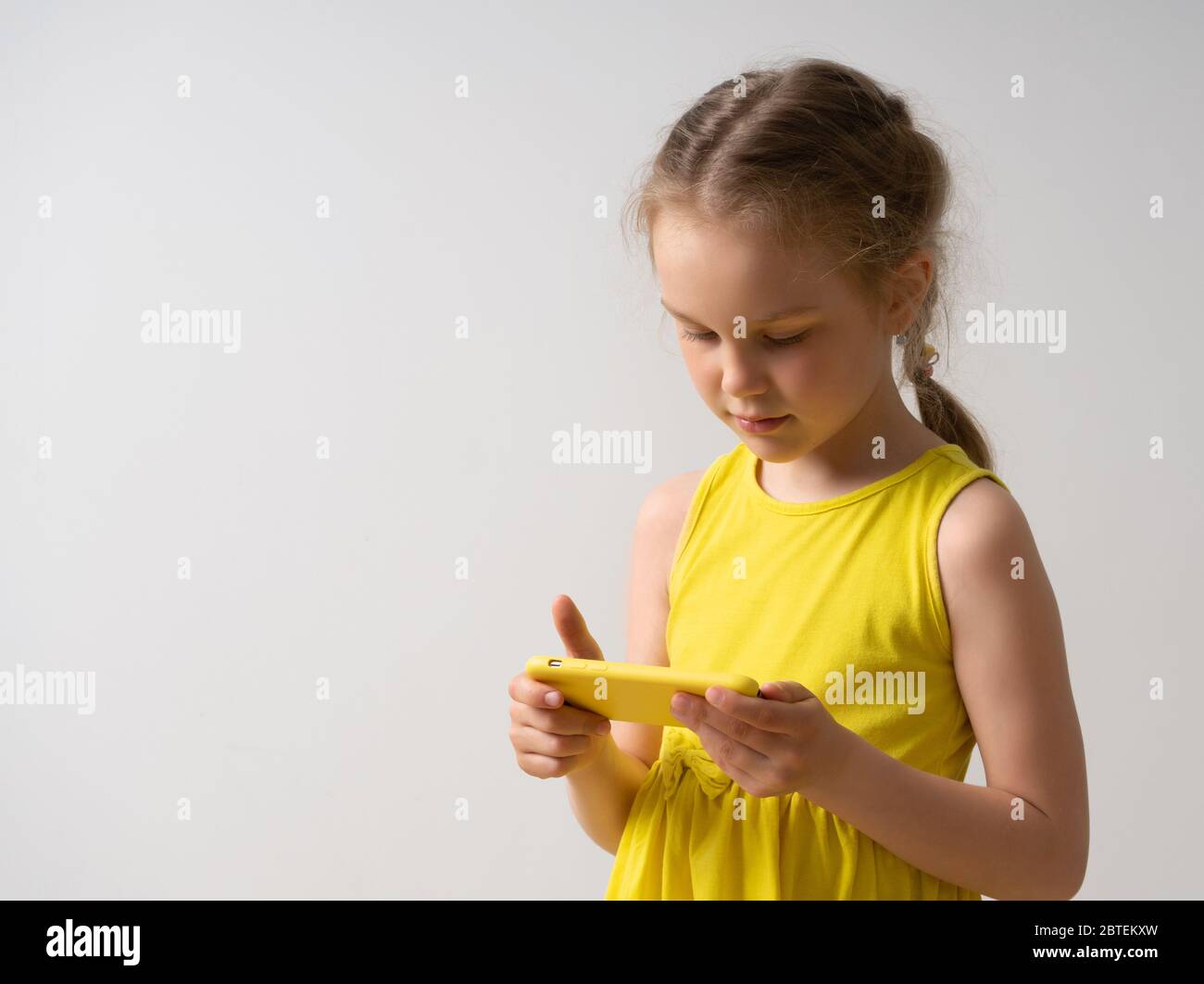 Schöne kleine Mädchen in hellen ärmellosen Kleid mit niedlichen Zopf genießt mit ihrem stilvollen smartpthone. Nahaufnahme Studio-Porträt isoliert auf weiß Stockfoto