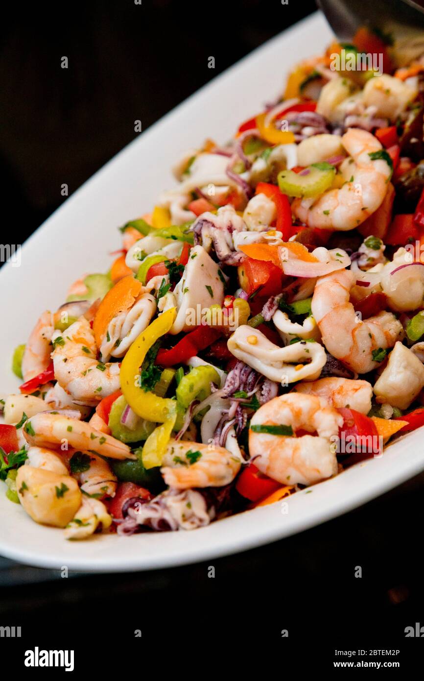 Meeresfrüchte-Buffet bei der Veranstaltung. Es bietet gemischten, gekochten Seafood-Salat auf einer großen weißen Platte, die darauf wartet, dass Gäste serviert werden. Stockfoto