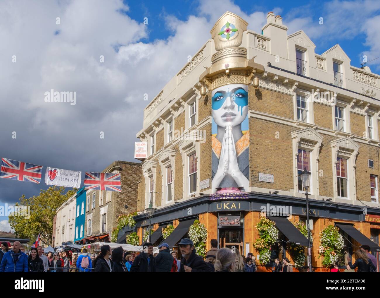 Menschenmassen, die auf dem Portobello Road Market einkaufen, mit japanischem Restaurant Ukai und Wandmalerei-Street Art Lady Kinoko von Fin DAC im Hintergrund. Stockfoto