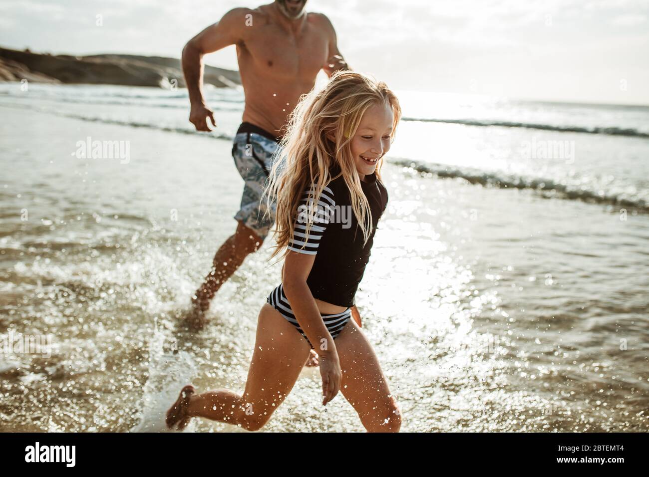 Nettes Mädchen läuft im Wasser mit ihrem Vater am Strand. Mädchen spielt am Strand mit ihrem Vater. Familie am Strand genießen. Stockfoto
