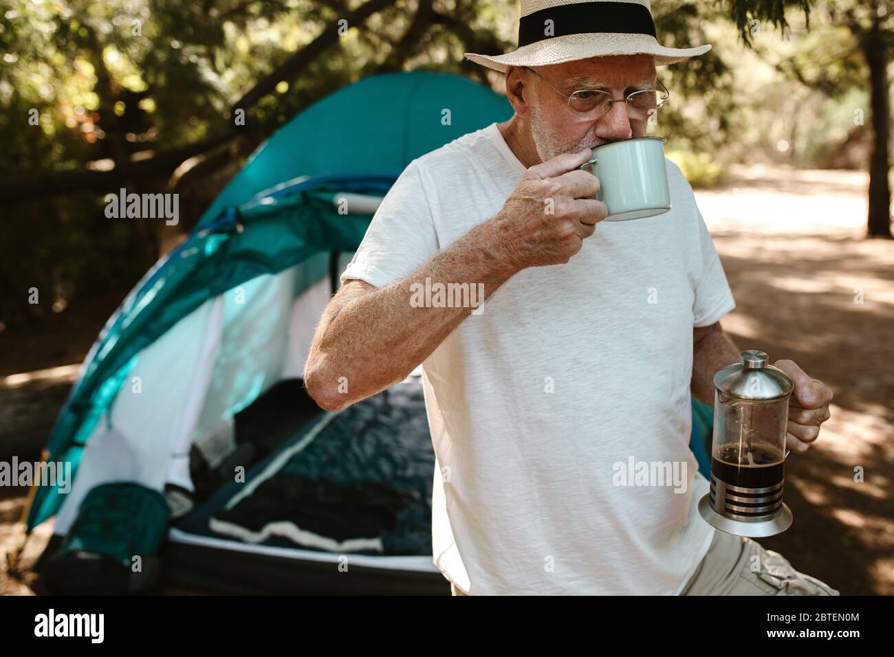 Älterer Mann beim Kaffee auf dem Campingplatz. Kaukasischer Mann camping in der Natur trinken Kaffee außerhalb des Zeltes. Stockfoto