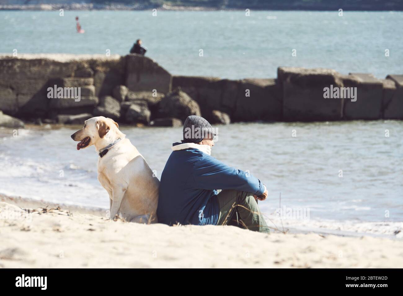 Der alte Mann und sein Hund, der sich an einem kleinen Strand in Lissabon, Portugal, zurücklehnen und auf das Meer schauen, sehen aus wie ein Fischer Stockfoto