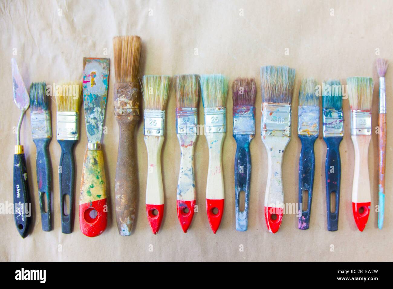 Schmutzige gebrauchte Künstlerpinsel liegen in einer Reihe oder Linie. Hintergrund beige Papier Kraft. Stockfoto