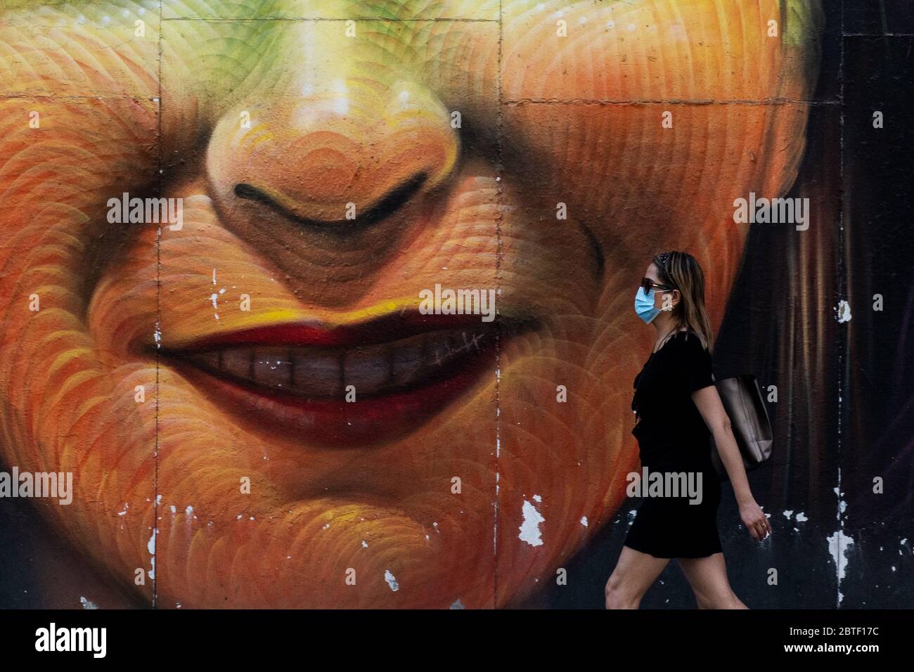 Madrid, Spanien. Mai 2020. Eine Frau, die eine schützende Gesichtsmaske trägt, geht an einem Wandgemälde in der Gran Via Straße vorbei. Madrid hat die sogenannte Phase-1-Transition von der Sperrung des Coronavirus betreten, die es vielen Geschäften ermöglicht, wieder zu eröffnen, sowie Restaurants, die Kunden im Freien bedienen. Quelle: Marcos del Mazo/Alamy Live News Stockfoto