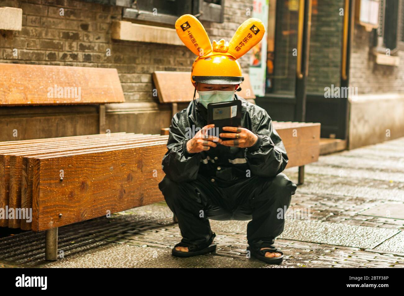 Ein Mitarbeiter von Meituan Dianping hockt sich mit seinem Telefon, während er auf seinen nächsten Job in Shanghais trendigem Viertel Xintiandi wartet. Stockfoto