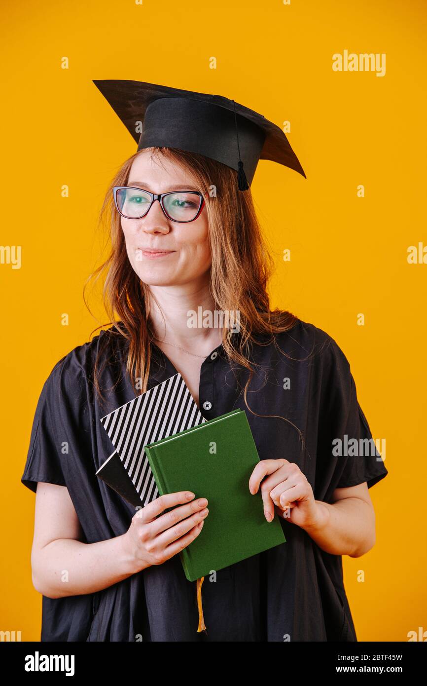 Mädchen in akademischer Kleidung und mit einem Diplom in den Händen auf einem gelben Hintergrund Stockfoto