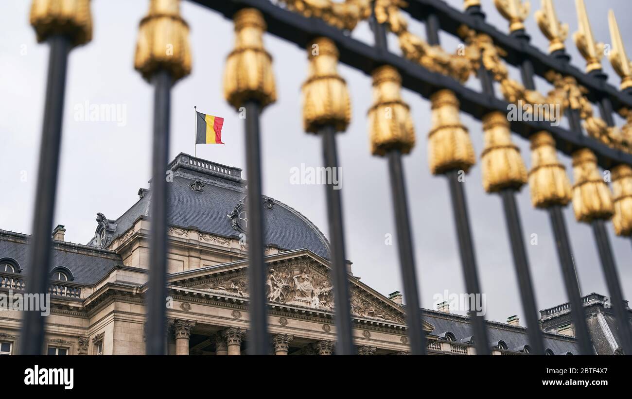 Der Königspalast in Brüssel, Belgien. Blick durch den Metallzaun mit goldenen Details. Nationalflagge des Königreichs Belgien winkt auf der Spitze. Stockfoto