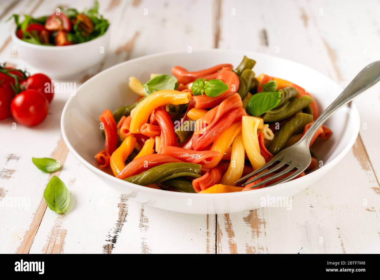 Italienische vegane bunte Penne Pasta in einem weißen Teller auf Holztisch. Nahaufnahme Stockfoto