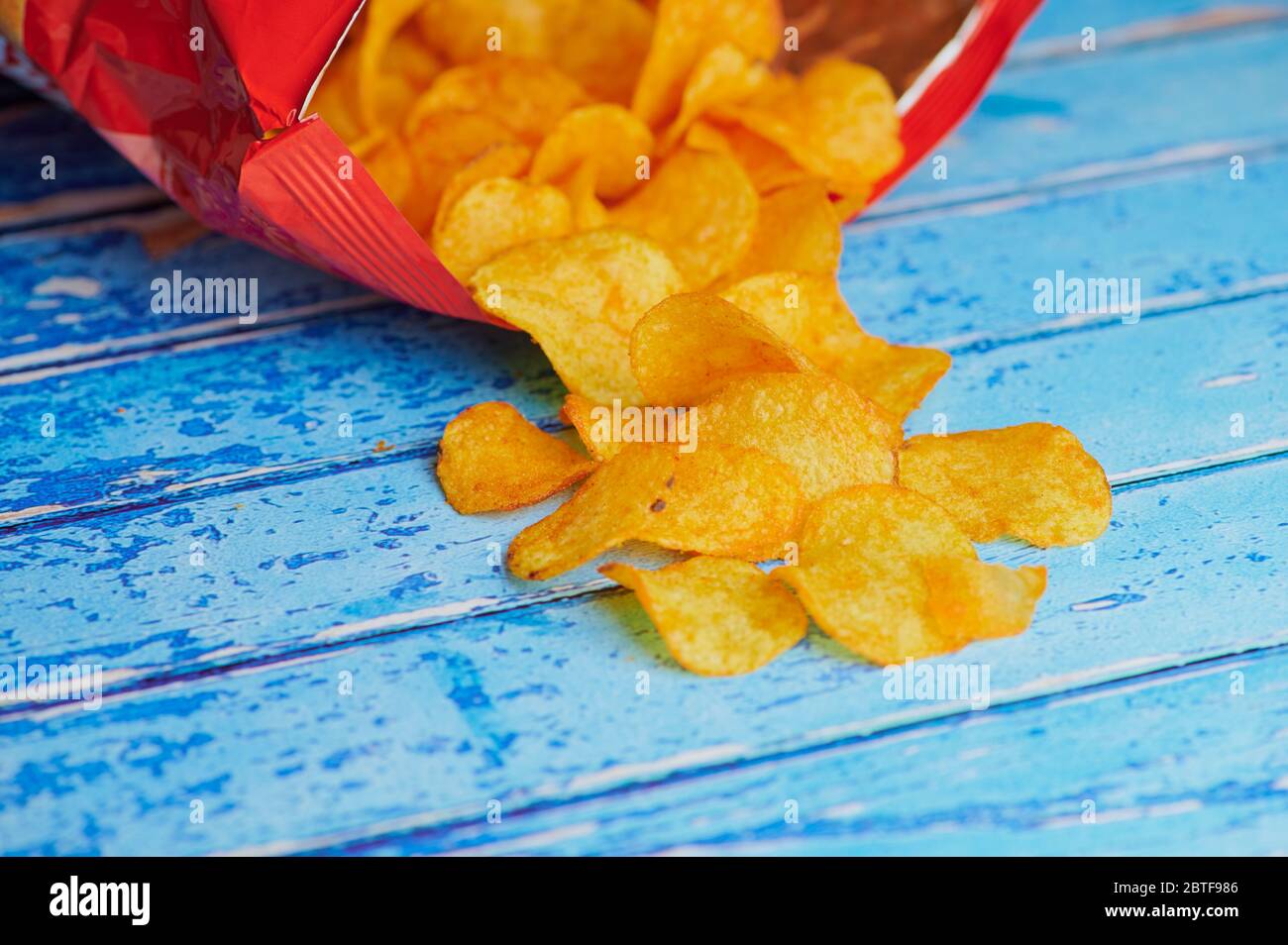 Kartoffelchips liegen vor einem Chips-Beutel vor blauem Hintergrund Stockfoto
