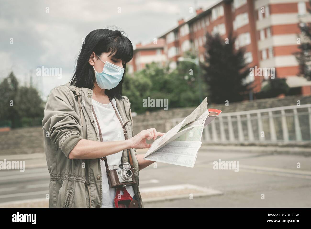 Frau mit medizinischer Maske mit Kamera Blick auf eine Karte der Stadt im Freien Stockfoto