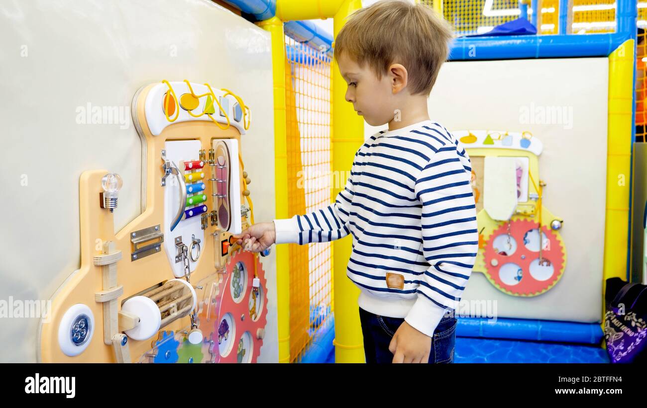 Niedlicher kleiner Junge, der mit Knöpfen und Knöpfen auf pädagogischem Kinderbrett im Kindergarten spielt Stockfoto