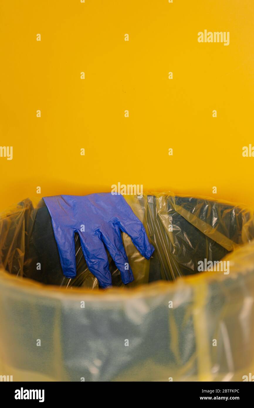 Werfen Sie den Einweghandschuh in den Behälter auf orangefarbener Hintergrundisolierung. Coronovirus Konzept. Stockfoto