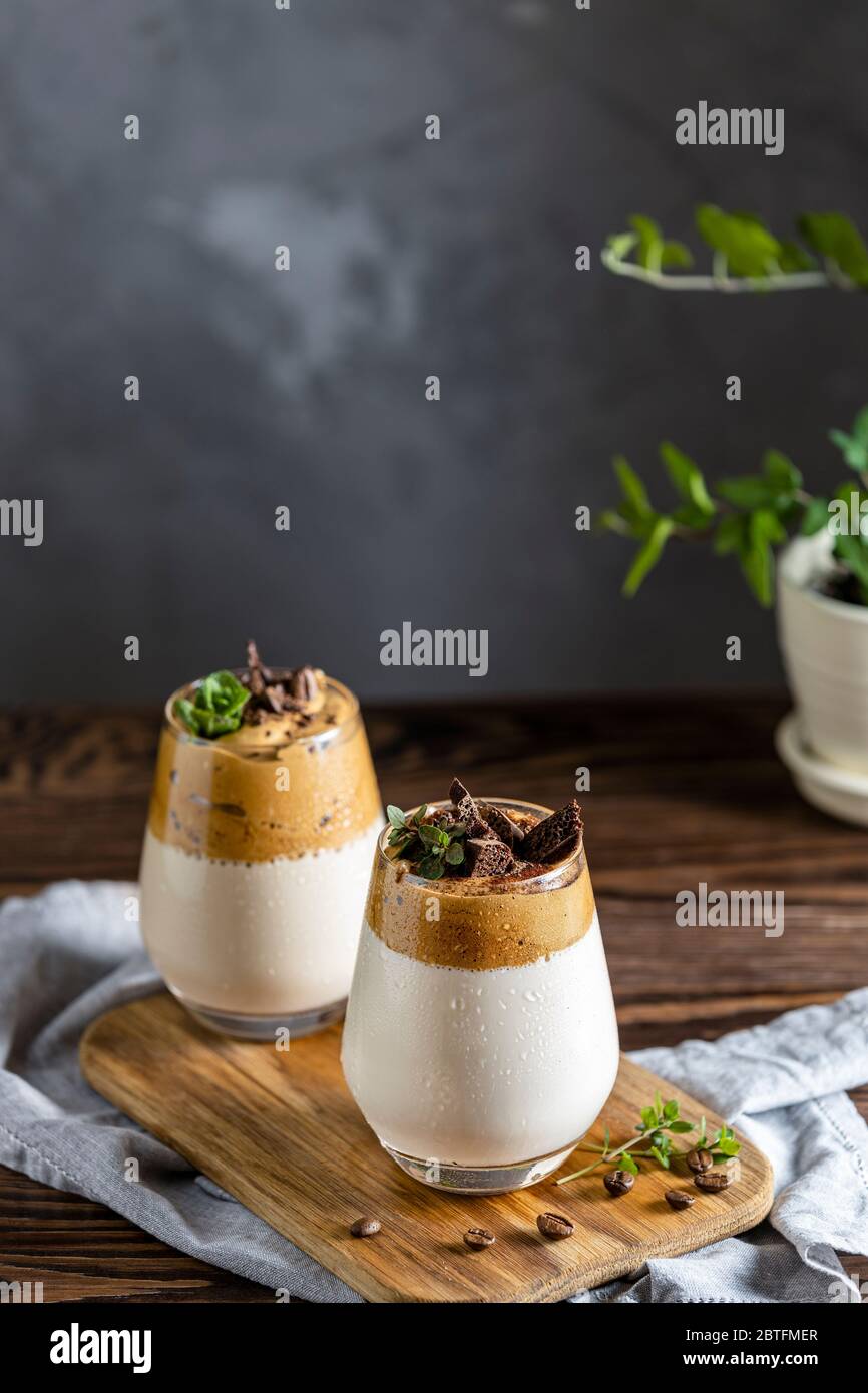 Zwei Gläser Iced Dalgona Coffee, ein trendiger, flauschiger, cremiger Schlagkaffee, dekoriert mit Thymian und dunkler Schokolade. Dunkler rustikaler Stil. Stockfoto