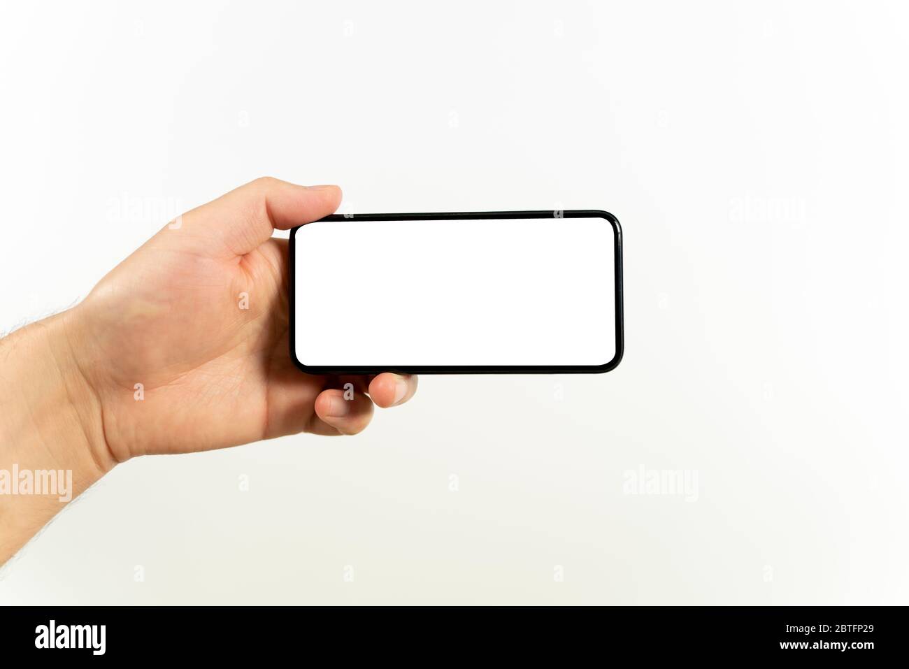 Mann Hand hält das schwarze Smartphone mit leerem Bildschirm und modernen rahmenlosen Design positioniert horizontal - isoliert auf weißem Hintergrund Stockfoto