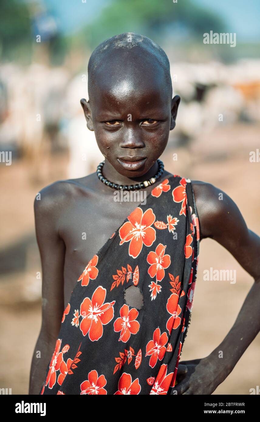 MUNDARI TRIBE, SÜDSUDAN - 11. MÄRZ 2020: Kind in traditionellem Gewand mit floralem Ornament, das die Hand auf der Taille hält und während des Lebens die Kamera betrachtet Stockfoto