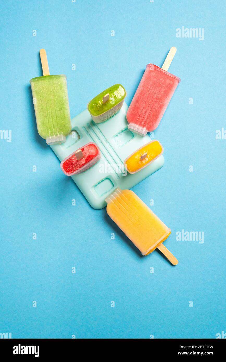 Hausgemachtes Eis in ihren Plastikformen auf blauem Hintergrund, oben gesehen. Eis mit frischem Obst. Stockfoto