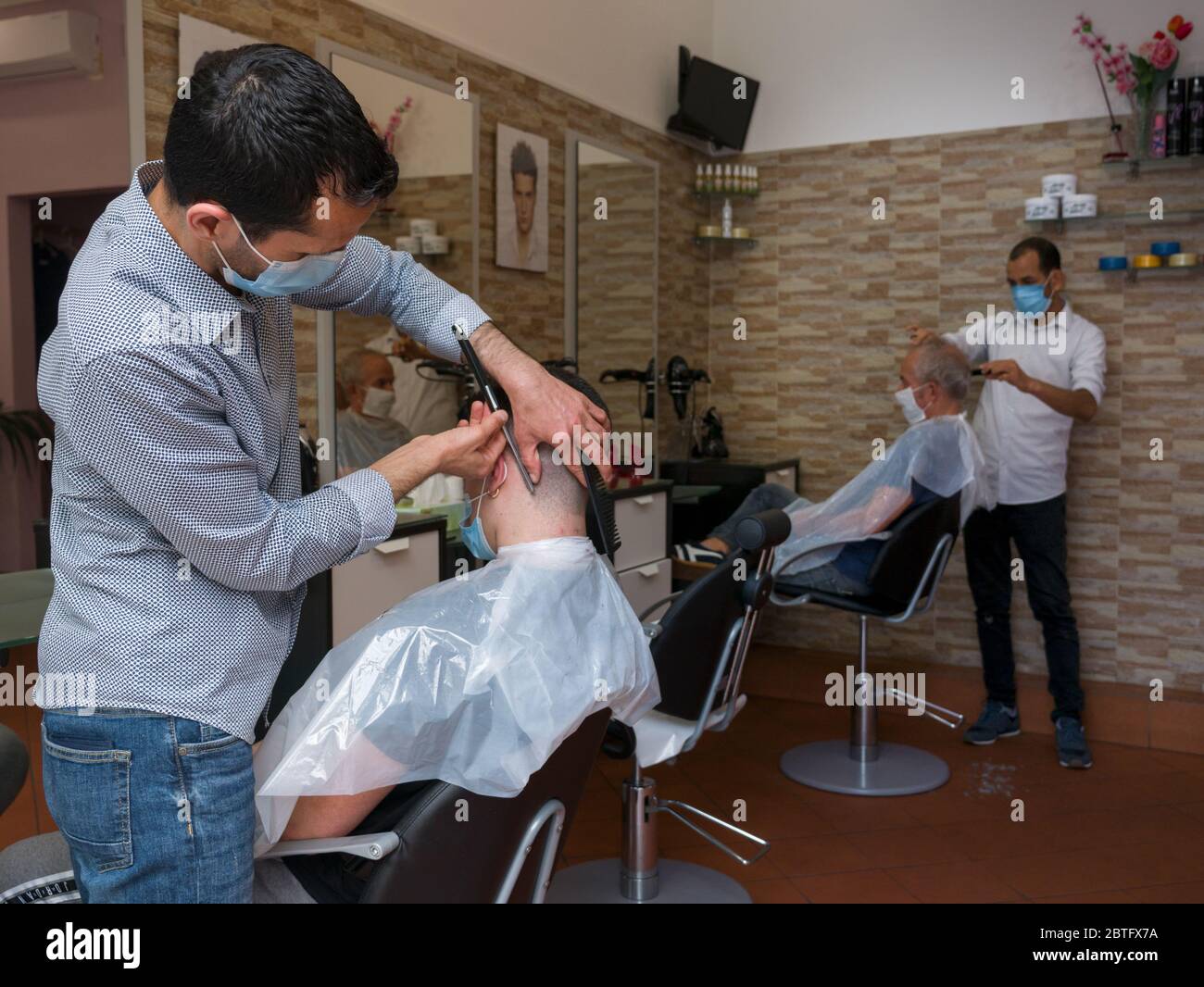 Florenz, Italien - 2020, Mai 18: Während der Sperrung von Covid-19 erhalten die Leute im Friseurladen einen Haarschnitt mit Schutzmaske. Stockfoto