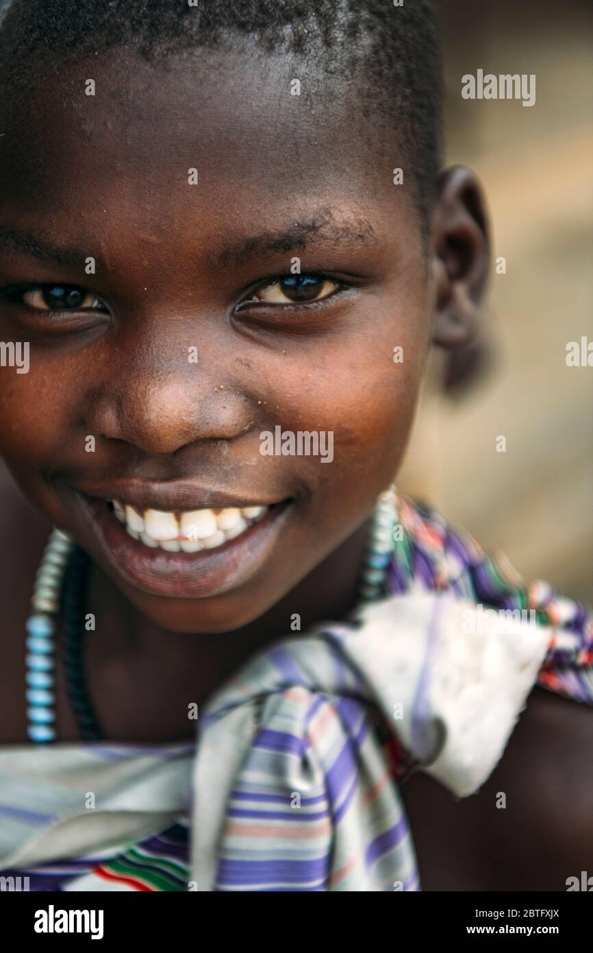 TOPOSA STAMM, SÜDSUDAN - 12. MÄRZ 2020: Mädchen in bunten Gewand mit Perlen lächelnd und Blick auf Kamera im Dorf Toposa Stamm im Süden Stockfoto