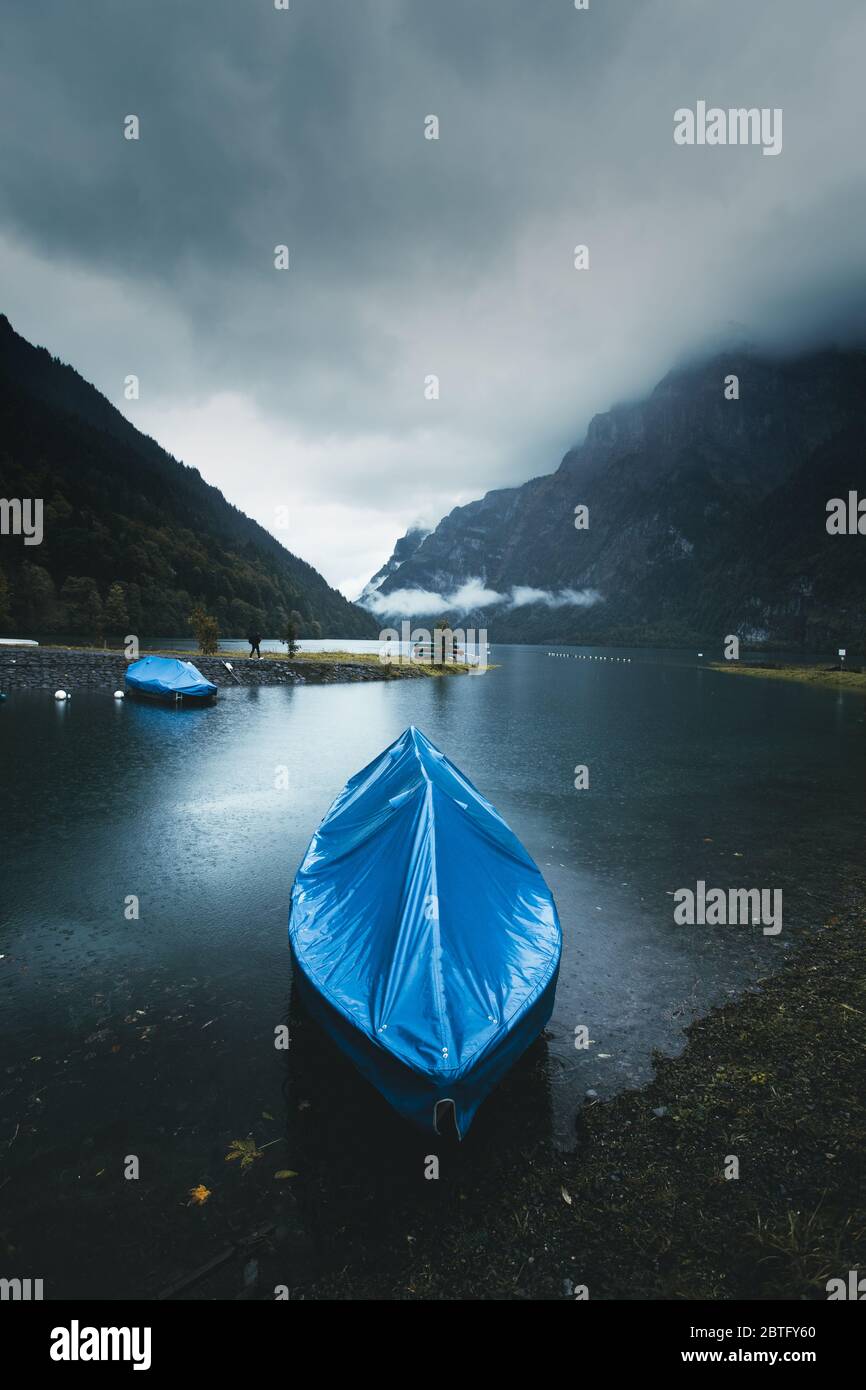Moody Landschaft eines Bootes in der Nähe des Ufers am Klontal See angedockt. Schöne stimmungsvolle dunkle Landschaft mit nebeligen Bergen im Hintergrund Stockfoto