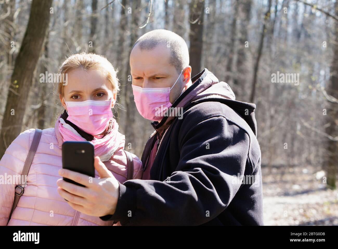 Mann und Frau in medizinischen Masken gehen und fotografieren im Wald während der Quarantäne. Stockfoto